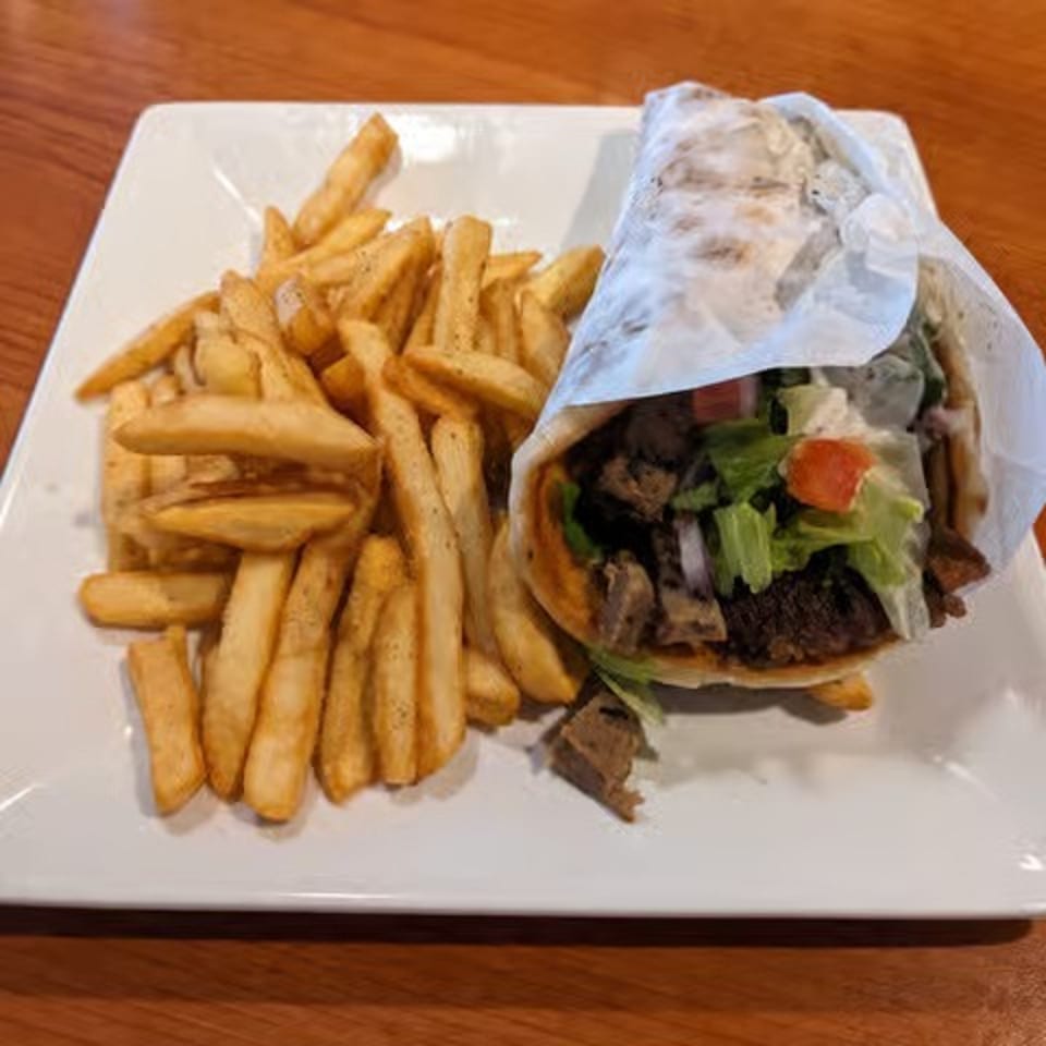 Burger wrapped in paper with lettuce and tomato, served alongside golden fries on a white plate.